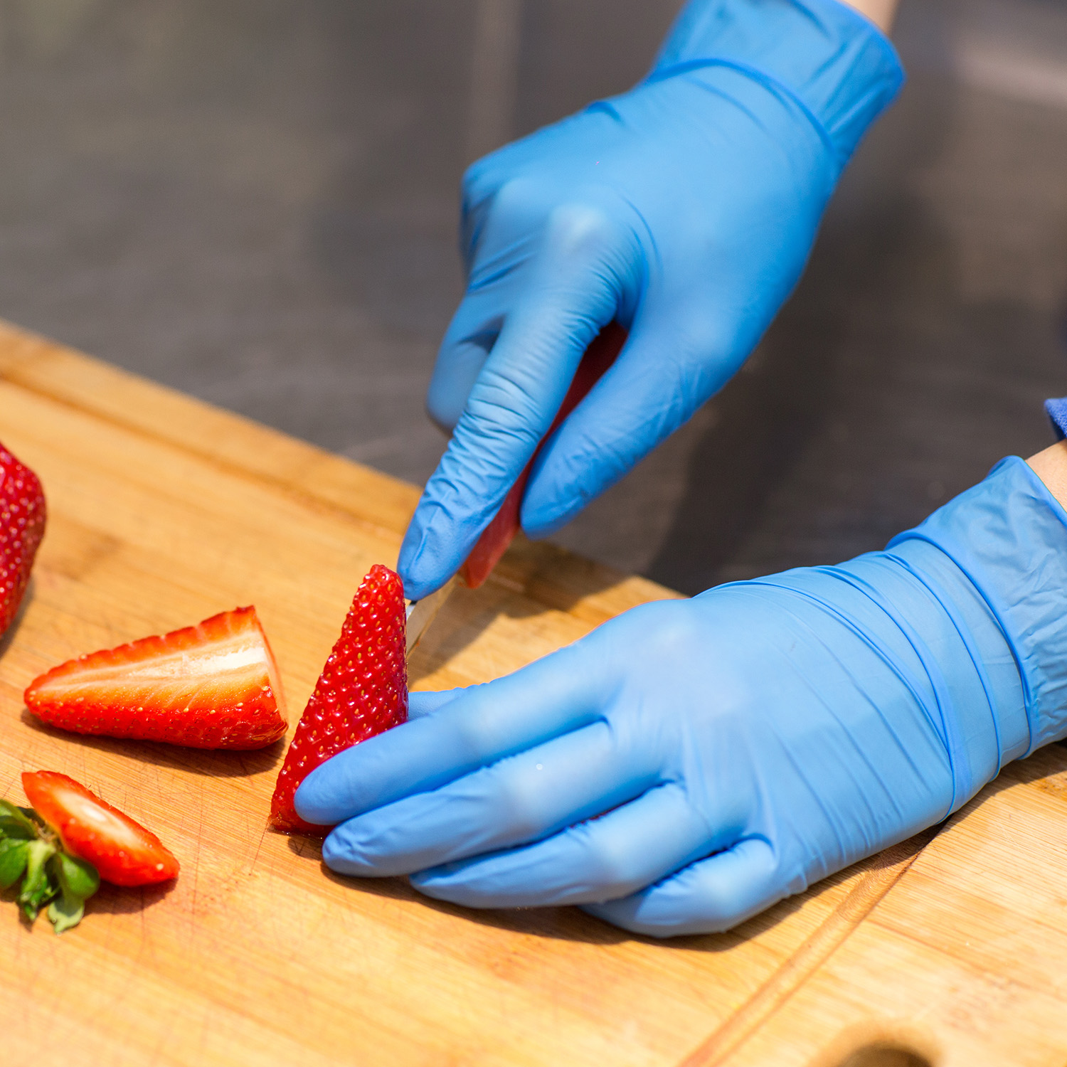 Gloved hands cutting strawberries.